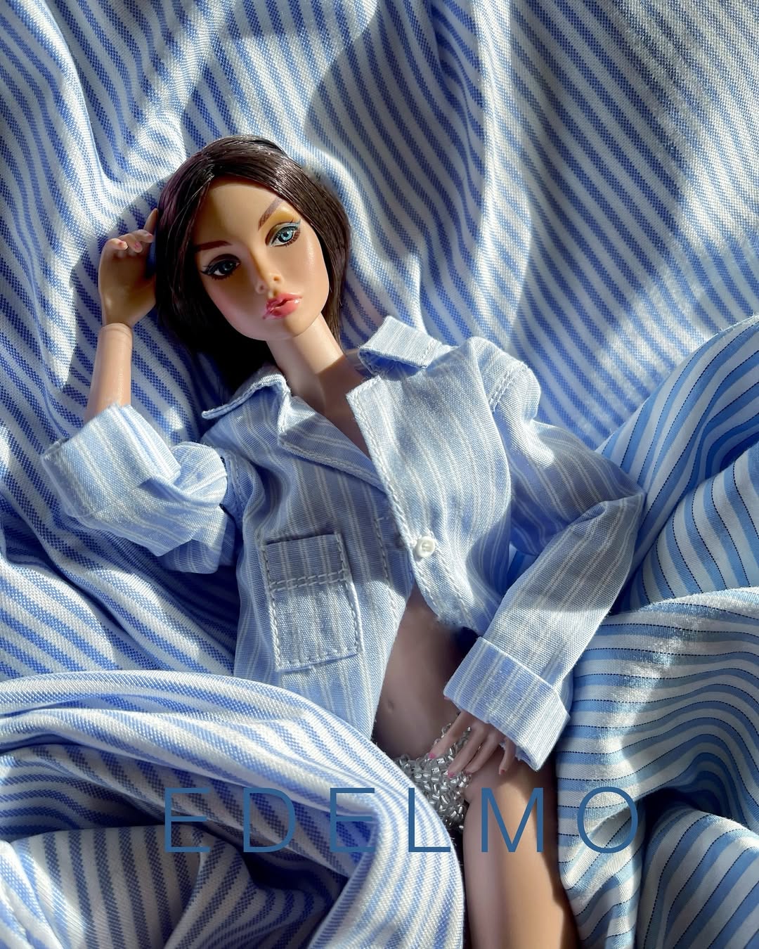Tina recostada sobre una tela de rayas azules en una composición de fotografía de muñecas
